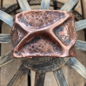 May include: A hammered copper bracelet with a textured surface. The bracelet is a wide cuff style and has a rustic, organic look.