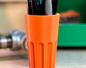 May include: Orange plastic pen holder with a ribbed design. The holder is filled with black, gray, and red pens.