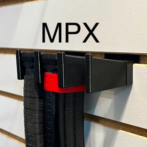 May include: Black plastic magazine holder with the text "MPX" on a white wall. Two black magazines with red accents are hanging on the holder.