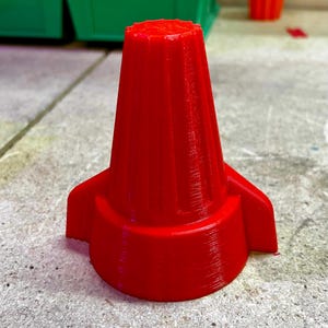 Könnte beinhalten: Ein leuchtend roter Drahtverbinder mit zwei seitlichen Flügeln. Der Verbinder hat ein geripptes Design und ist aus Kunststoff.
