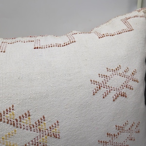 May include: White throw pillow with a geometric pattern in brown and yellow thread. The pattern is a repeating design of stylized stars.
