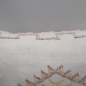 May include: White throw pillow with a geometric pattern in shades of red, yellow, and orange. The pillow has a fringed edge.