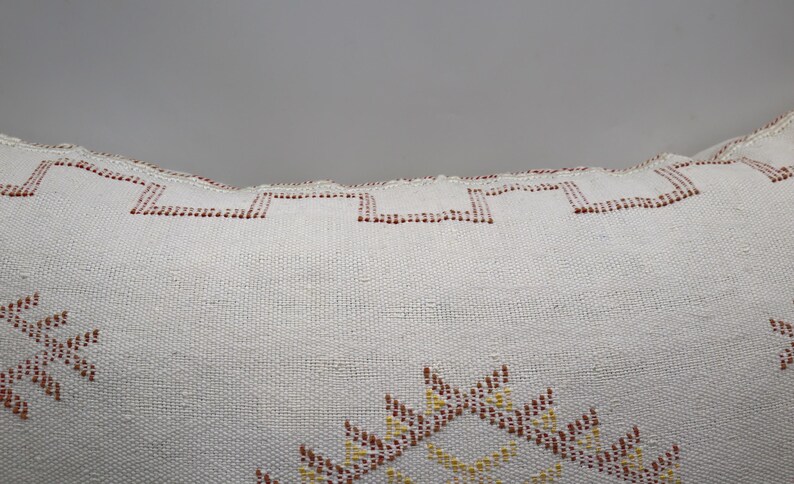 May include: White throw pillow with a geometric pattern in shades of red, yellow, and orange. The pillow has a fringed edge.