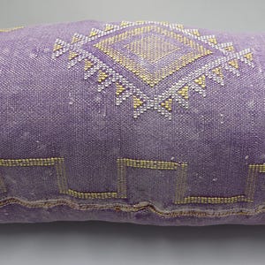 Puede incluir: Un coj&iacute;n de tiro de color morado y dorado con un dise&ntilde;o geom&eacute;trico. El coj&iacute;n est&aacute; hecho de una tela suave y tejida.