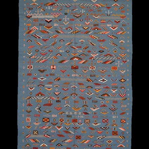 May include: A rectangular, blue rug with a complex geometric pattern. The design incorporates various shapes and colors, including red, orange, yellow, and white, creating a visually rich textile. The rug has a fringe along the bottom edge.
