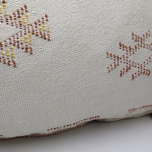 May include: A white throw pillow with a brown and yellow geometric pattern. The pillow has a zipper closure and a tassel.