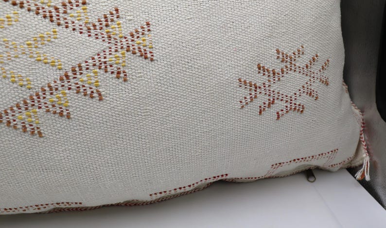 May include: A white throw pillow with a brown and yellow geometric pattern. The pillow has a zipper closure and a tassel.