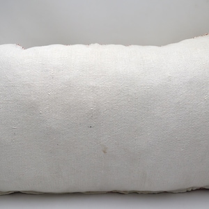 May include: A white rectangular pillow with a red and white trim. The pillow is made of a soft, woven fabric.
