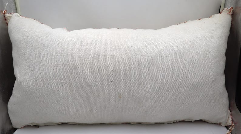 May include: A white rectangular pillow with a red and white trim. The pillow is made of a soft, woven fabric.