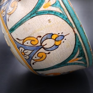 May include: A white ceramic bowl with a blue, green, and yellow floral design. The bowl has a crackled glaze and is slightly tilted.