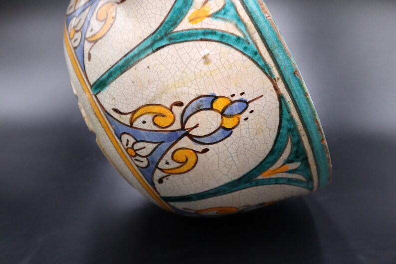 May include: A white ceramic bowl with a blue, green, and yellow floral design. The bowl has a crackled glaze and is slightly tilted.