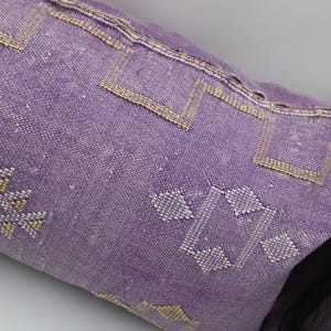 Puede incluir: Una almohada morada con un patr&oacute;n geom&eacute;trico en hilo blanco y amarillo. La almohada est&aacute; hecha de una tela suave y tejida.