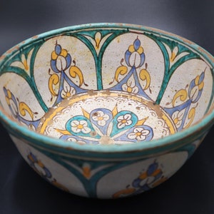 May include: A white ceramic bowl with a blue, green, and yellow floral design. The bowl has a wide rim and a rounded bottom.