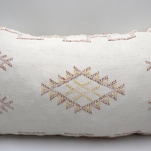 May include: White throw pillow with a geometric pattern in shades of red, yellow, and brown. The pillow is made of a soft, woven fabric and has a subtle texture.