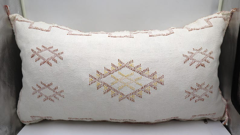 May include: White throw pillow with a geometric pattern in shades of red, yellow, and brown. The pillow is made of a soft, woven fabric and has a subtle texture.
