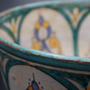 May include: Close-up of a ceramic bowl with a turquoise rim and intricate floral designs in blue, yellow, and white.