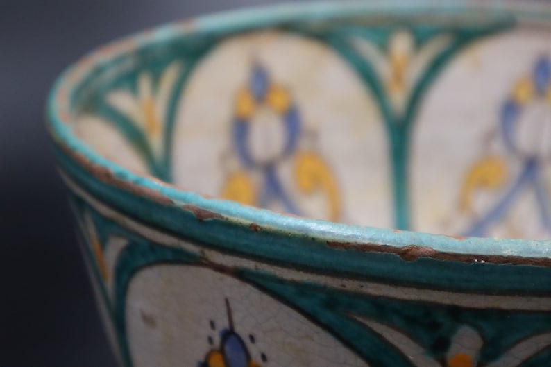 May include: Close-up of a ceramic bowl with a turquoise rim and intricate floral designs in blue, yellow, and white.