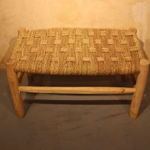 Puede incluir: Un banco de mimbre tejido con un marco de madera natural. El banco tiene una forma rectangular y está hecho de materiales naturales.