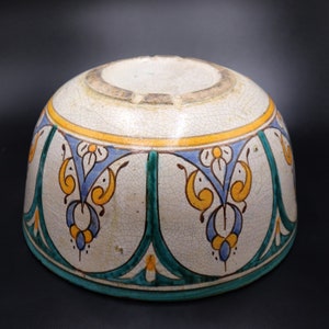 May include: A white ceramic bowl with a blue, green, and yellow floral design. The bowl has a rounded shape and a slightly flared rim.