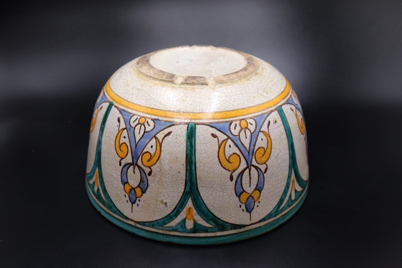May include: A white ceramic bowl with a blue, green, and yellow floral design. The bowl has a rounded shape and a slightly flared rim.