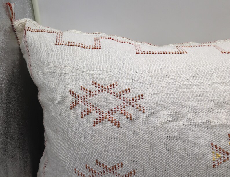 May include: White throw pillow with a geometric pattern in shades of brown. The pillow has a woven texture and a fringed edge.