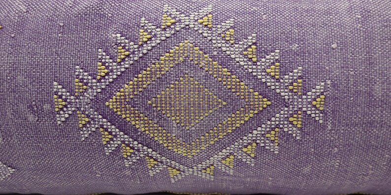 Puede incluir: Almohada morada con un patr&oacute;n geom&eacute;trico amarillo y blanco.