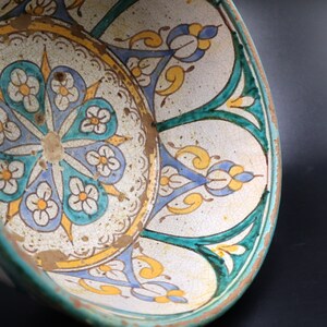 May include: A ceramic bowl with a white background and a colorful floral design. The bowl has a green rim and a blue and yellow floral pattern.