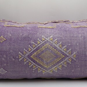 Puede incluir: Una almohada de tiro de color morado y dorado con un dise&ntilde;o geom&eacute;trico. La almohada est&aacute; hecha de una tela suave y tejida y tiene un aspecto desgastado sutil.