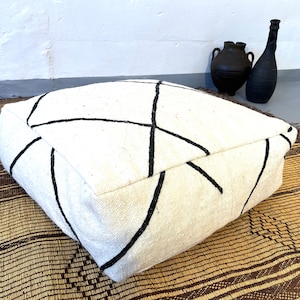 May include: White floor cushion with black geometric pattern. The cushion is sitting on a brown woven rug.