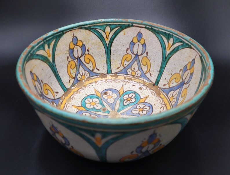 May include: A white ceramic bowl with a blue, green, and yellow floral design. The bowl has a wide rim and a rounded bottom.