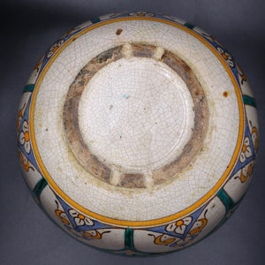May include: A white ceramic bowl with a blue, green, and yellow floral design. The bowl has a crackled glaze and a brown rim.