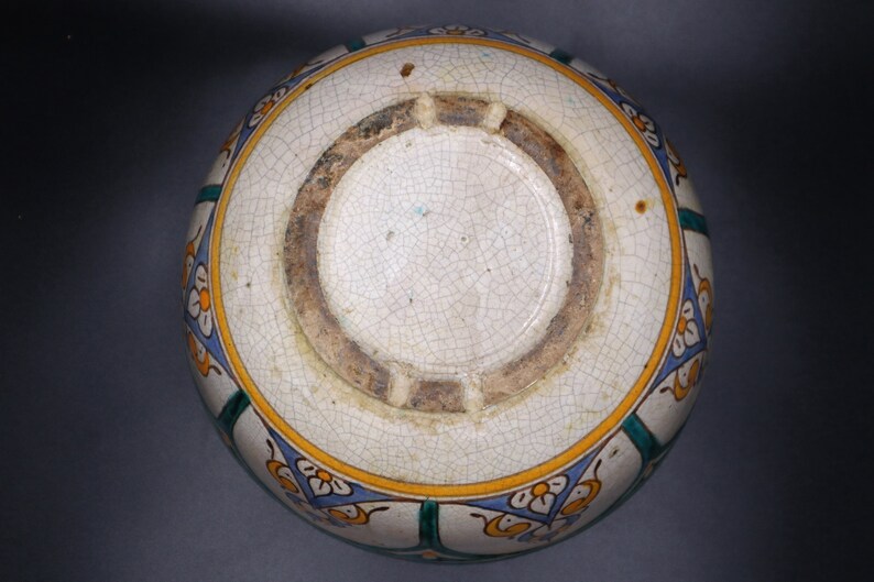 May include: A white ceramic bowl with a blue, green, and yellow floral design. The bowl has a crackled glaze and a brown rim.