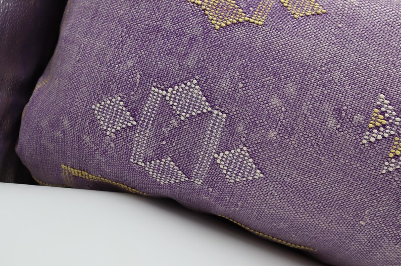 Puede incluir: Coj&iacute;n de tiro morado con un patr&oacute;n geom&eacute;trico blanco y amarillo.