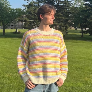 May include: A colorful striped sweater with a white base and pastel pink, yellow, and blue stripes. The sweater has a crew neck and long sleeves.