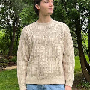 Può includere: Un maglione beige a maniche lunghe con un motivo a spina di pesce verticale, scollo rotondo e polsini e orlo a coste. Il maglione è abbinato a jeans azzurri e presenta un design a maglia testurizzata sul busto e sulle maniche.