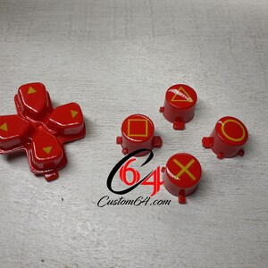 May include: Red and yellow PlayStation controller buttons. The buttons are shaped like a cross, square, circle, triangle, and X. The buttons are for a video game console.