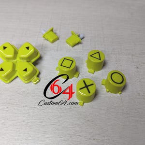 Può includere: Un set di pulsanti di ricambio gialli per un controller per videogiochi. I pulsanti presentano i simboli standard del pad direzionale: su, giù, sinistra, destra, cerchio, croce, quadrato e triangolo.