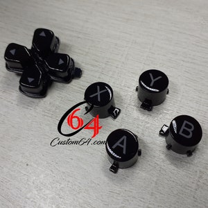 May include: A set of black replacement buttons for a video game controller. The buttons are labelled with the letters A, B, X, and Y. The buttons are designed to fit a standard controller.