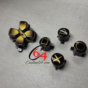 Op de afbeelding: Set van zes zwarte en gouden PlayStation-controllerknoppen. De knoppen hebben de standaard PlayStation-symbolen: vierkant, cirkel, driehoek, kruis en de directionele pad. De knoppen zijn ontworpen voor gebruik met een PlayStation-controller.