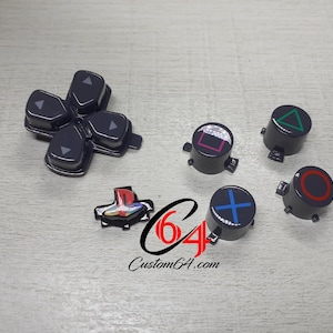 Op de afbeelding: Zwarte PlayStation 4 controllerknoppen en D-pad. De knoppen bevatten een vierkant, een driehoek, een cirkel en een kruis, elk met een andere kleur. De D-pad is zwart. De website Custom64.com is ook zichtbaar.