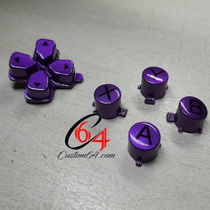 May include: Purple replacement buttons for a video game controller. The buttons are labeled with the letters X, Y, A, and B, and the directional buttons are labeled with arrows. The buttons are made of a shiny, metallic material.