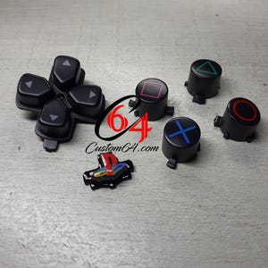 Puede incluir: Un conjunto de seis botones de repuesto negros para un mando de PlayStation. Los botones presentan varios símbolos, incluyendo un círculo, un triángulo, un cuadrado, una cruz y flechas direccionales.