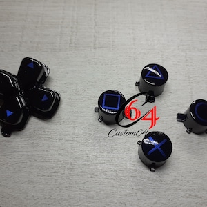 May include: A set of six black PlayStation controller buttons with blue symbols. The buttons include the directional pad, square, circle, triangle, cross, and a circle.