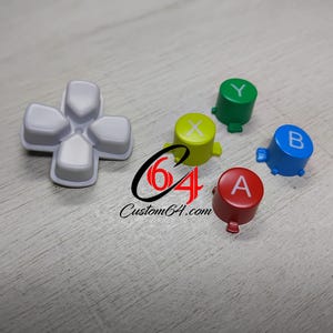 May include: A selection of brightly coloured video game controller buttons, including red, green, blue, and yellow, with the letters A, B, X, and Y. A grey directional pad is also present. The text "64 Custom64.com" is visible.