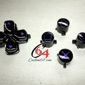 Peut inclure: Ensemble de boutons de manette PlayStation noirs avec des symboles violets. Les boutons comprennent le pavé directionnel, le carré, le cercle, le triangle et la croix.