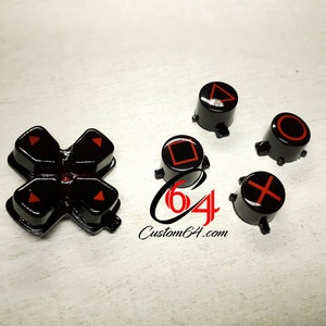 Peut inclure: Boutons de manette PlayStation noirs et rouges. Les boutons sont disposés en forme de croix avec les boutons directionnels au centre et les quatre boutons de face qui les entourent. Les boutons sont tous noirs avec des symboles rouges.