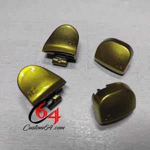 May include: Four gold-colored controller buttons, labeled "L2", "R2", "L1", and "R1". The buttons have a metallic finish and are arranged on a light gray surface. The Custom64.com logo is visible.