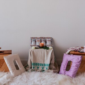 a cozy and inviting scene with a white rug, wooden crates, and various decorative items. There are two white pots, one on each side of the image, and a wooden crate with a pink pot on top. A wooden table is also present, with a vase and a candle placed on it. The arrangement of the objects creates a warm and welcoming atmosphere.