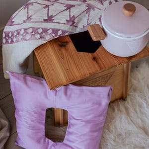 a wooden stool with a white pot on top, a purple pillow, and a wooden box with a lid, all placed on a white shag rug.