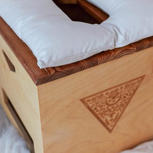 A wooden box with a white pillow on top, placed on a white furry surface.